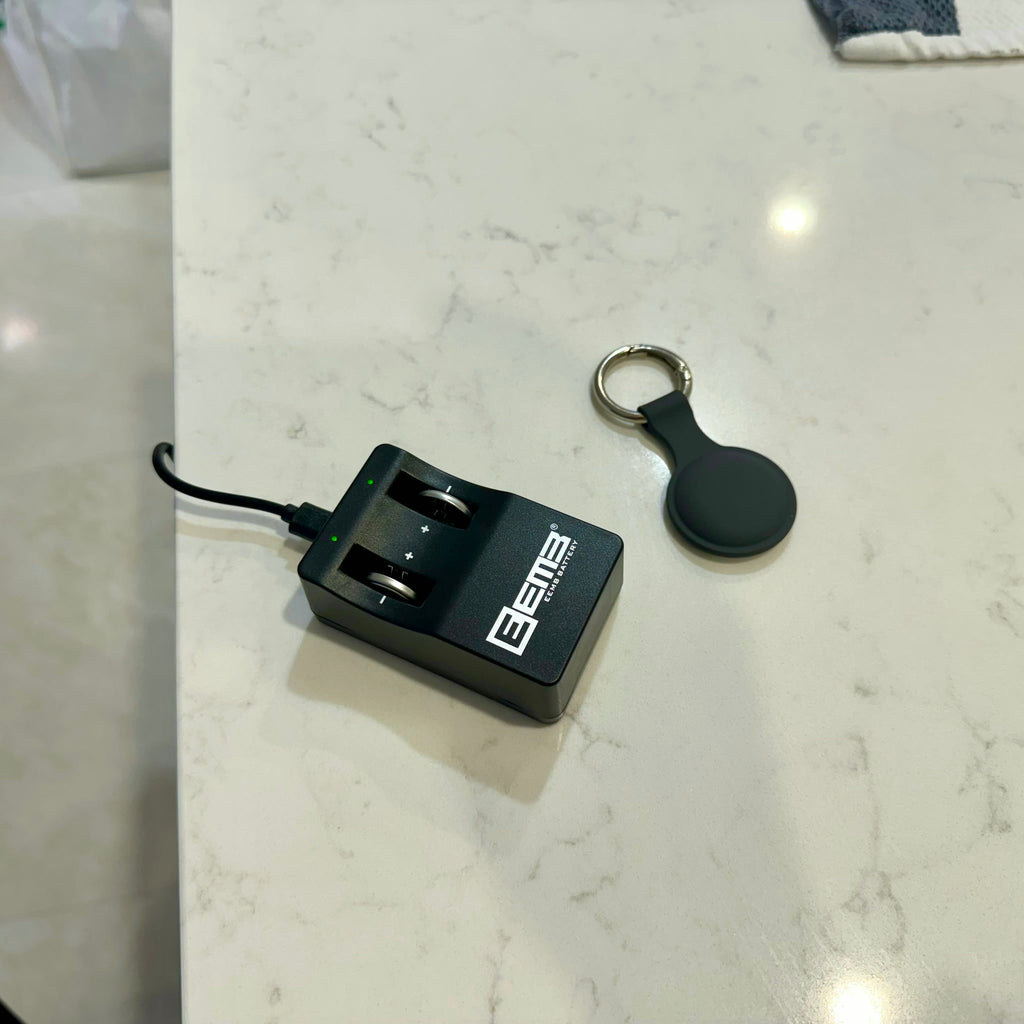 LIR2032 battery charger plugged in next to a key finder tracking tag on a kitchen bench