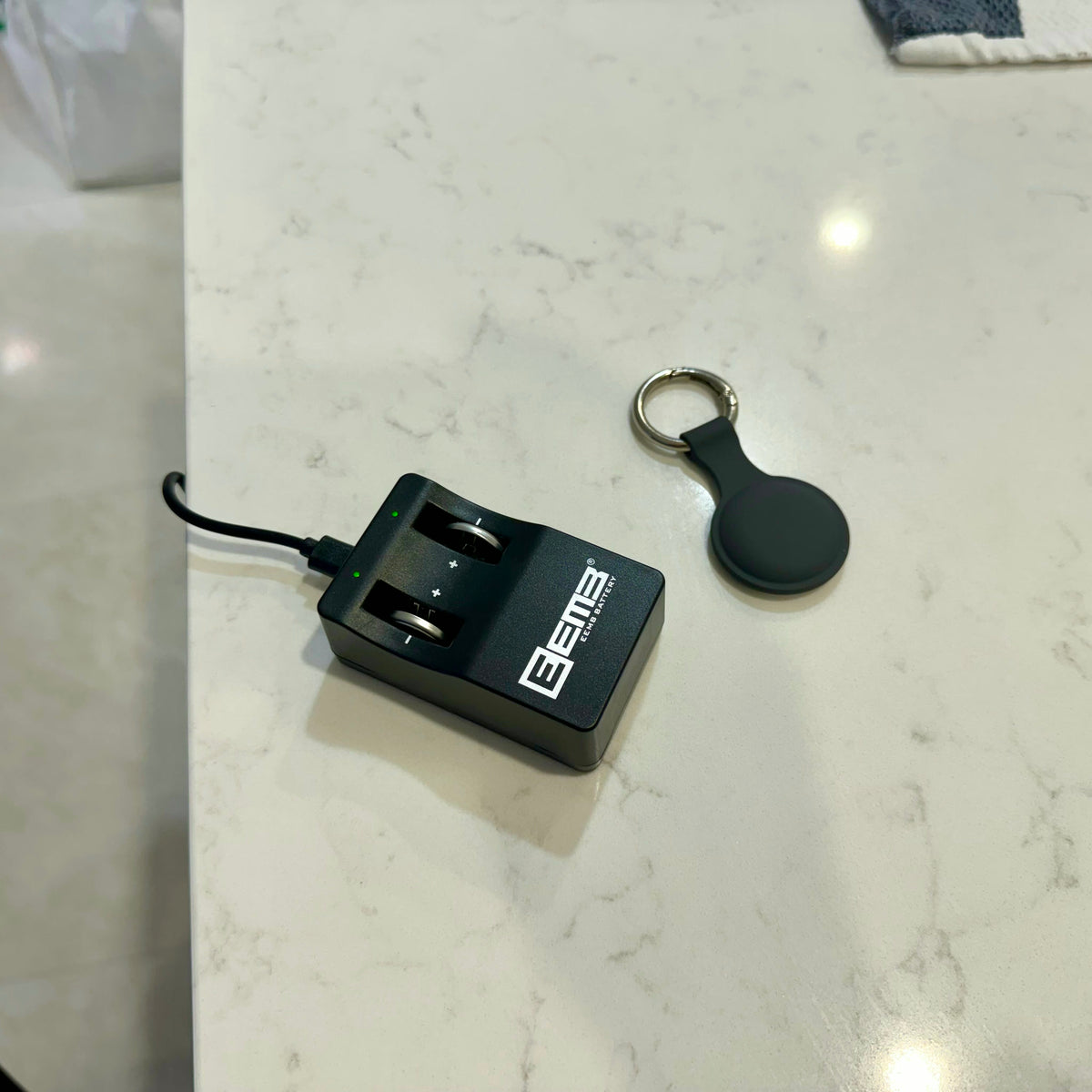 LIR2032 battery charger plugged in next to a key finder tracking tag on a kitchen bench