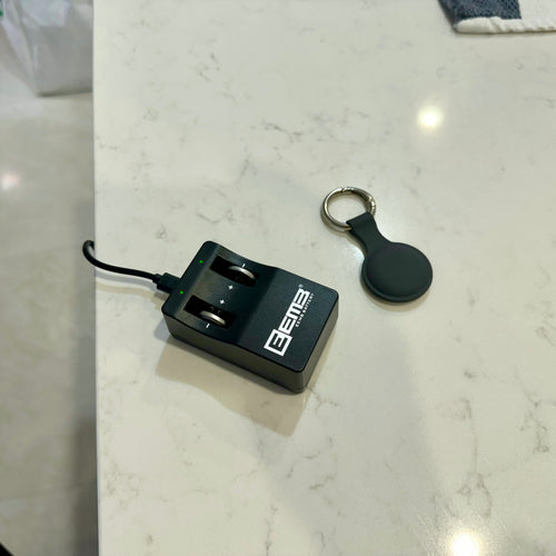 LIR2032 battery charger plugged in next to a key finder tracking tag on a kitchen bench