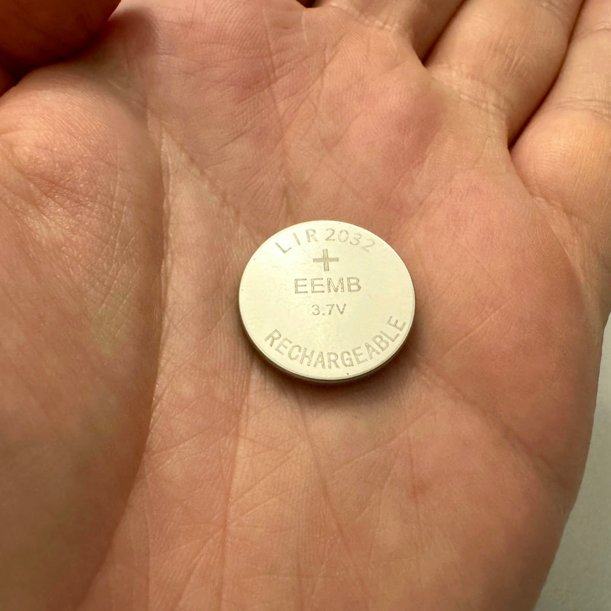 LIR2032 rechargeable coin cell battery held in palm of hand for size comparison, same size as CR2032